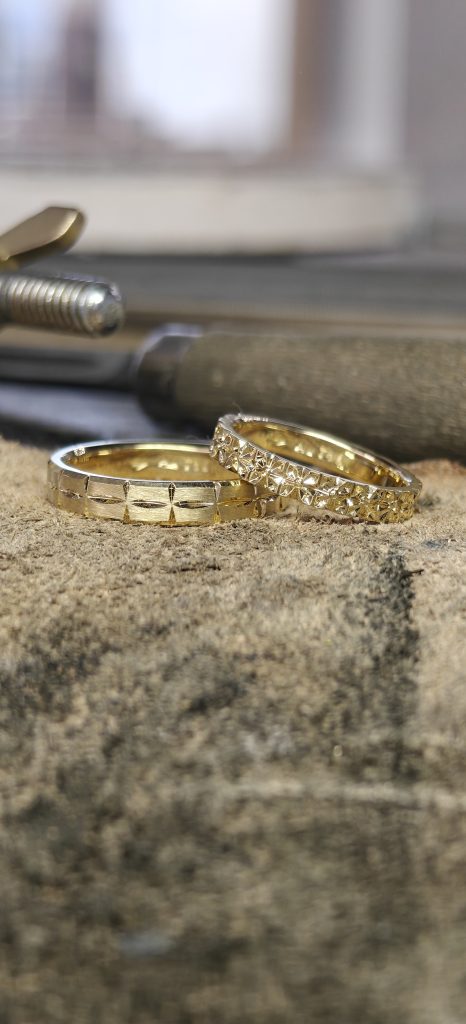 Unbearbeiteter Goldring während der handwerklichen Herstellung, auf einem Gravurblock mit Goldschmiedewerkzeugen im Hintergrund